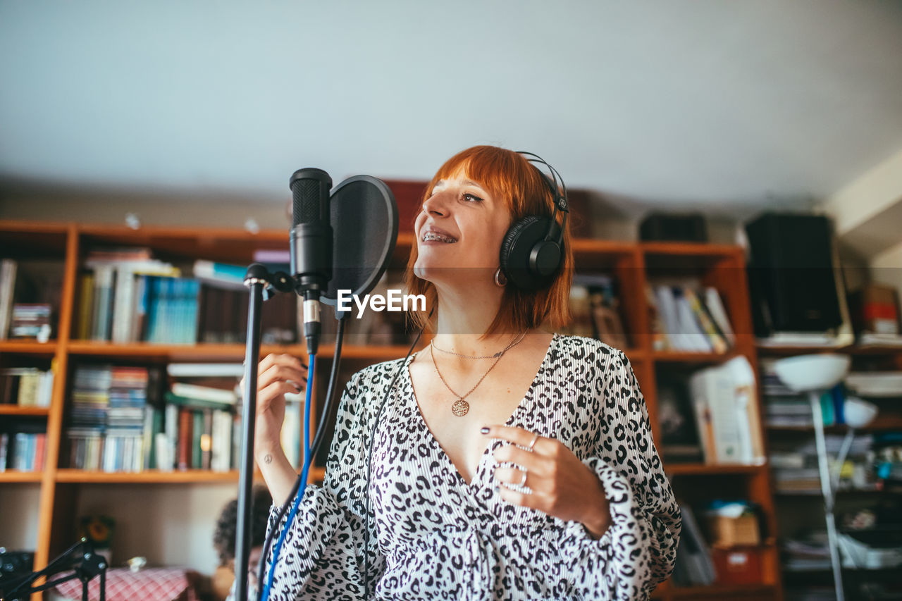 Female vocalist in headset singing song into mic with pop filter during record process at home