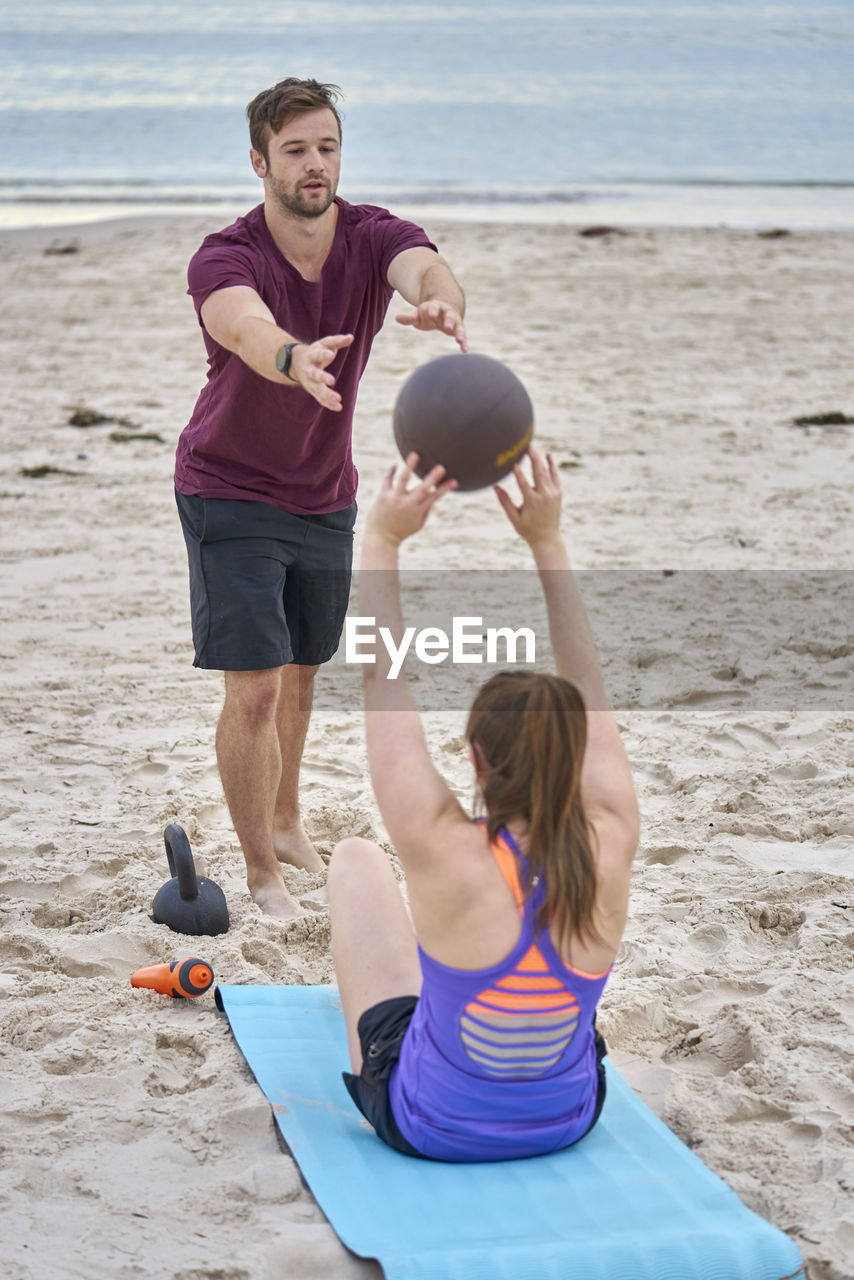 Young woman exercising with fitness instructor at beach