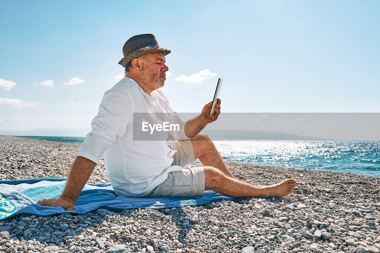 side view of woman sitting on beach against sky