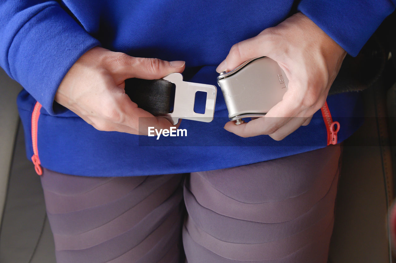 MIDSECTION OF WOMAN HOLDING CAMERA WHILE STANDING AGAINST BLUE