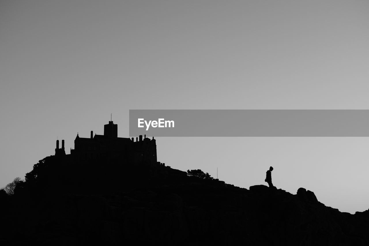 Low angle view of silhouette building on mountain against clear sky