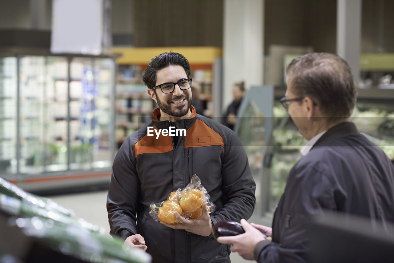 Mature man and sales clerk talking while holding vegetables at supermarket