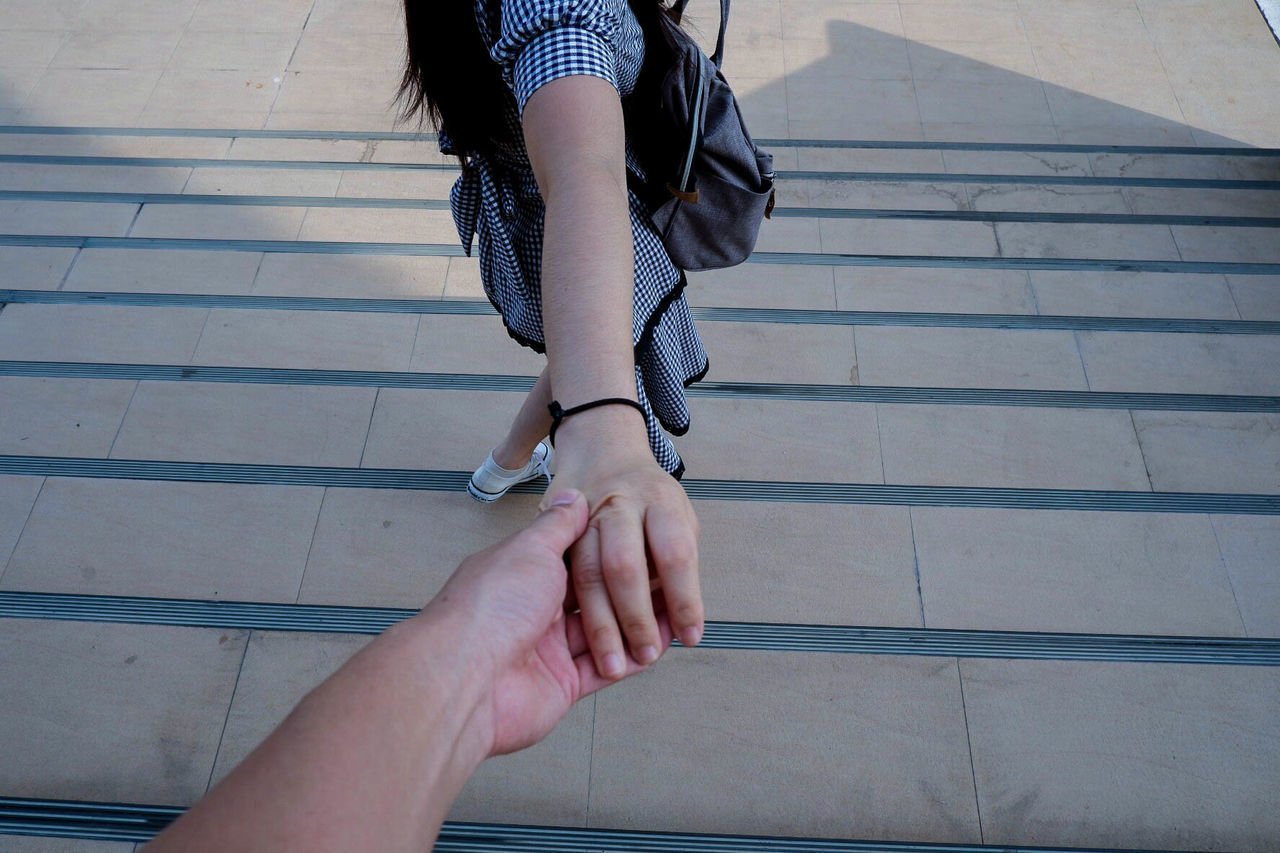 Cropped image of boyfriend holding girlfriend hand standing on steps