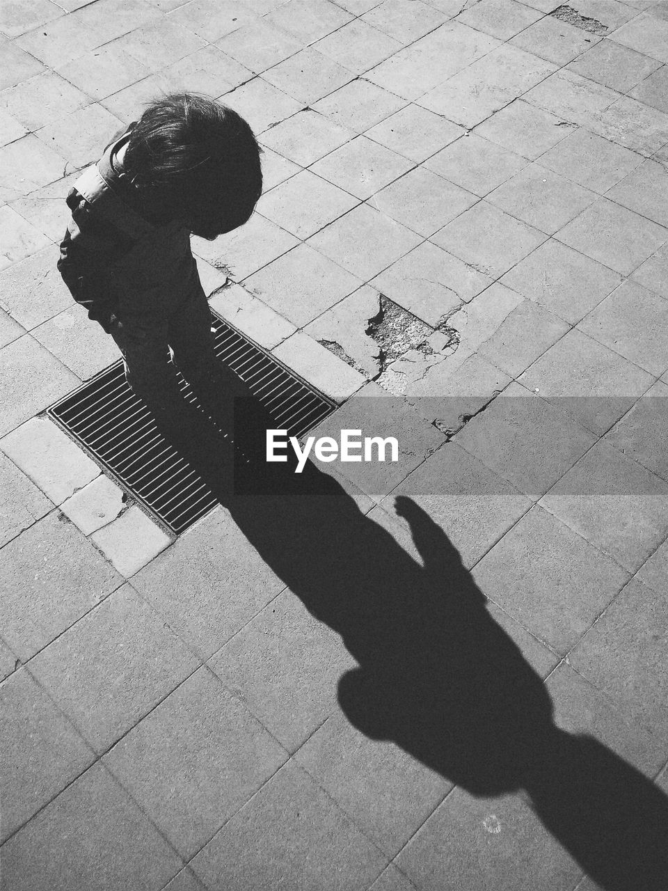 High angle view of boy standing on metal grate amidst paving street during sunny day