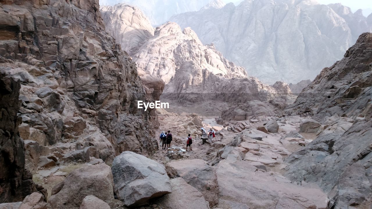 PEOPLE ON ROCKS BY MOUNTAIN