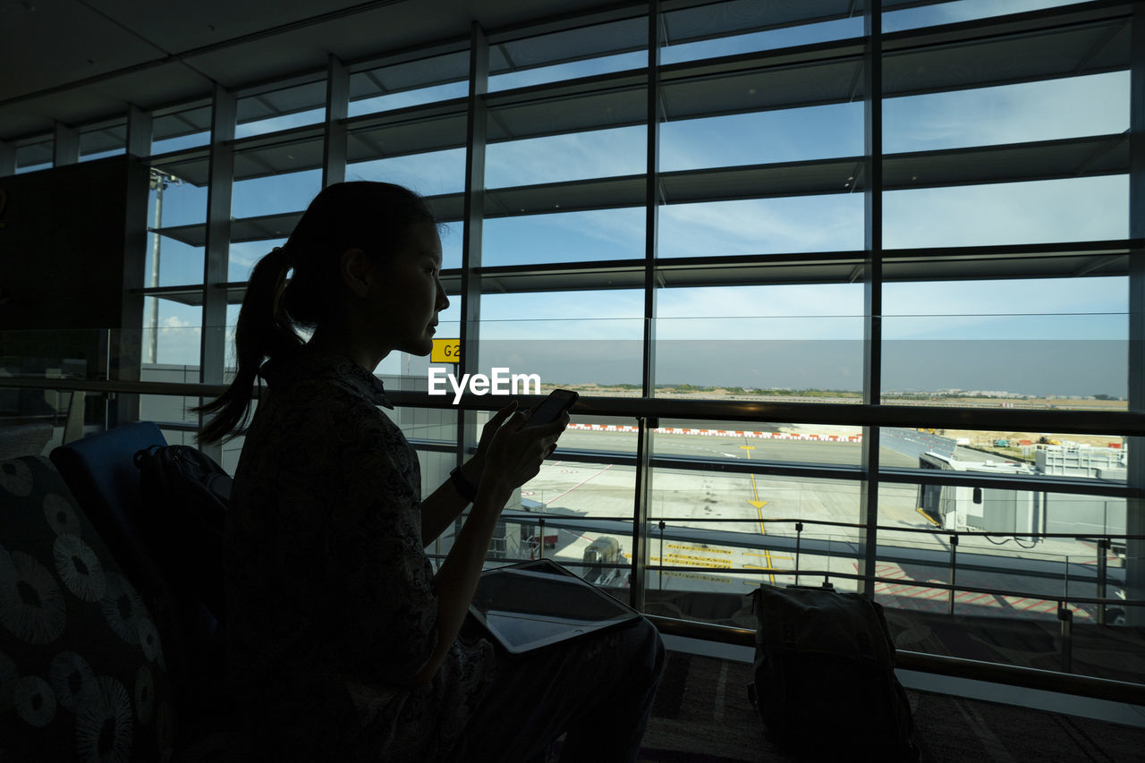 Side view of woman looking through window at airport