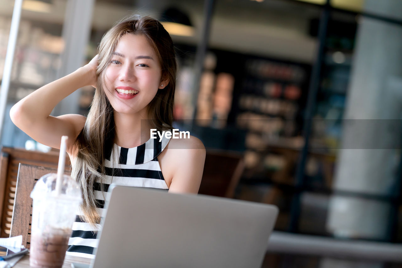 PORTRAIT OF A SMILING YOUNG WOMAN USING PHONE