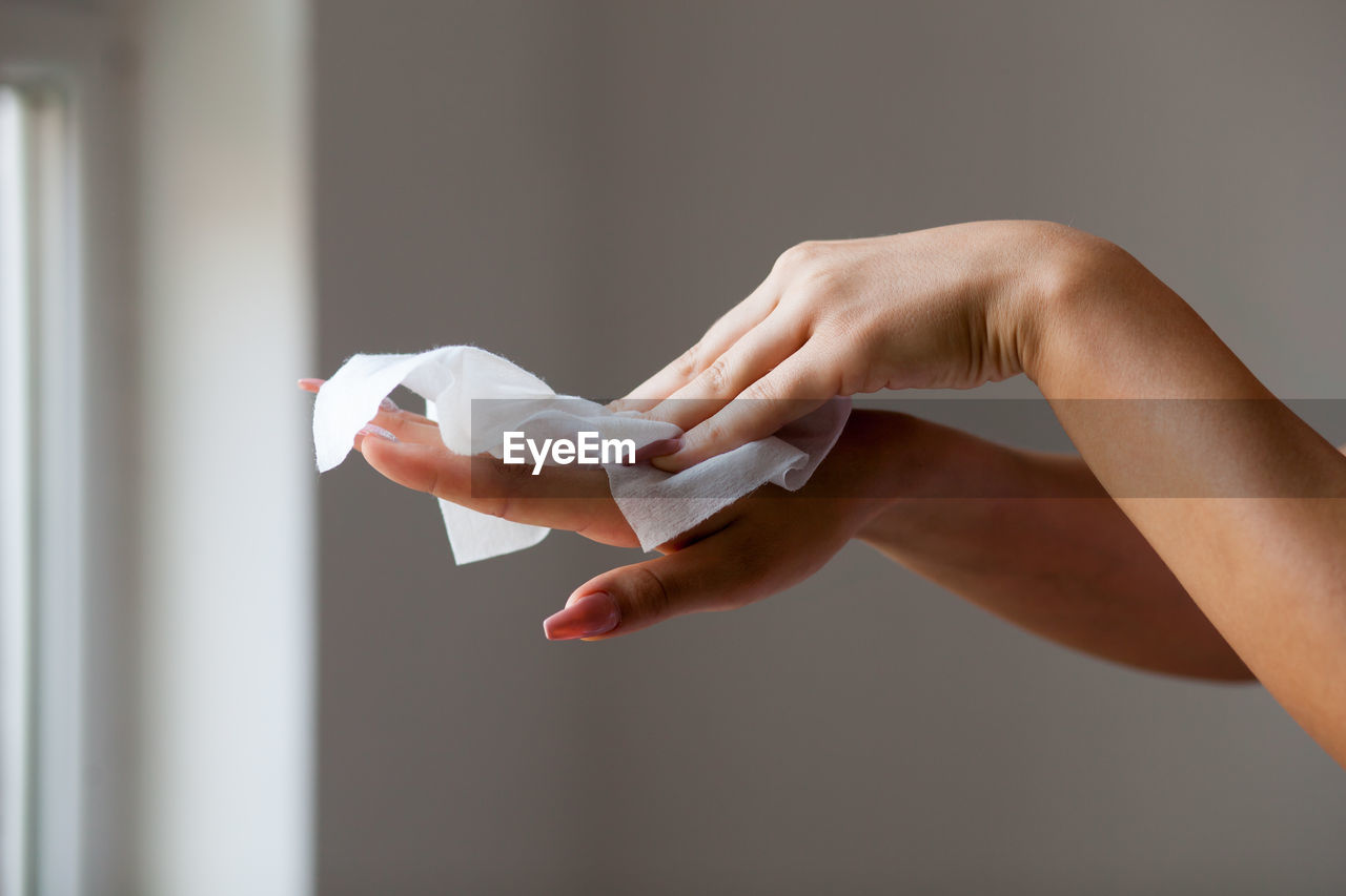 Cropped image of woman cleaning hands with tissue paper at home