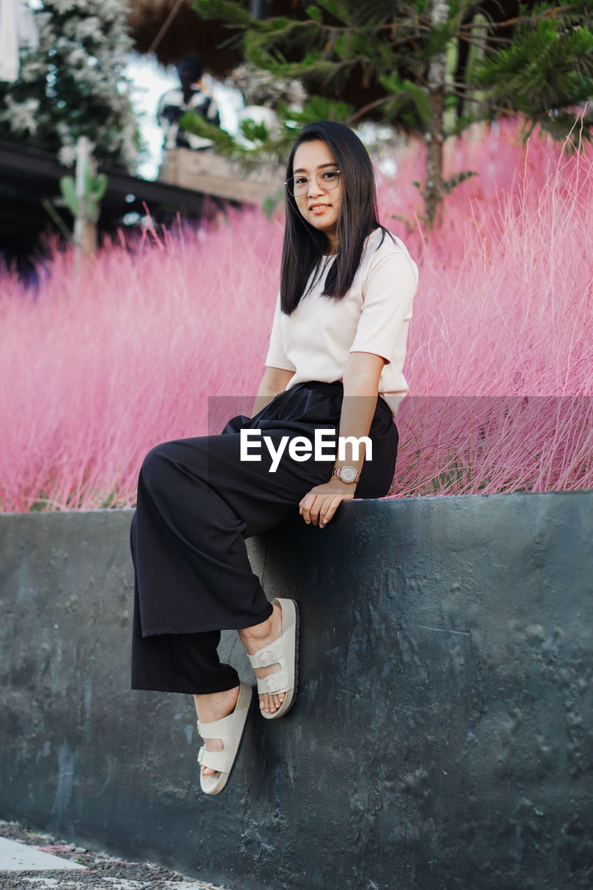 Portrait of young woman sitting on retaining wall
