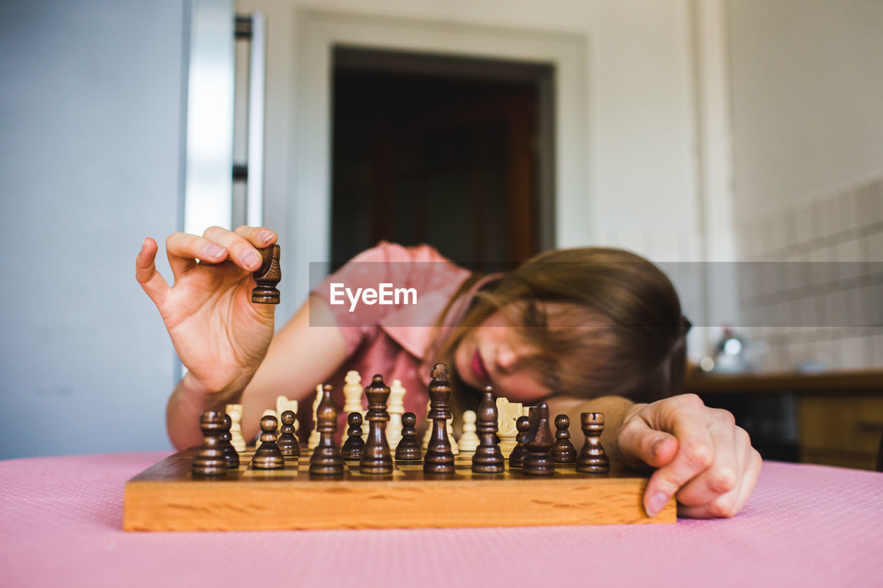 Portrait of blonde girl playing chess on table at home