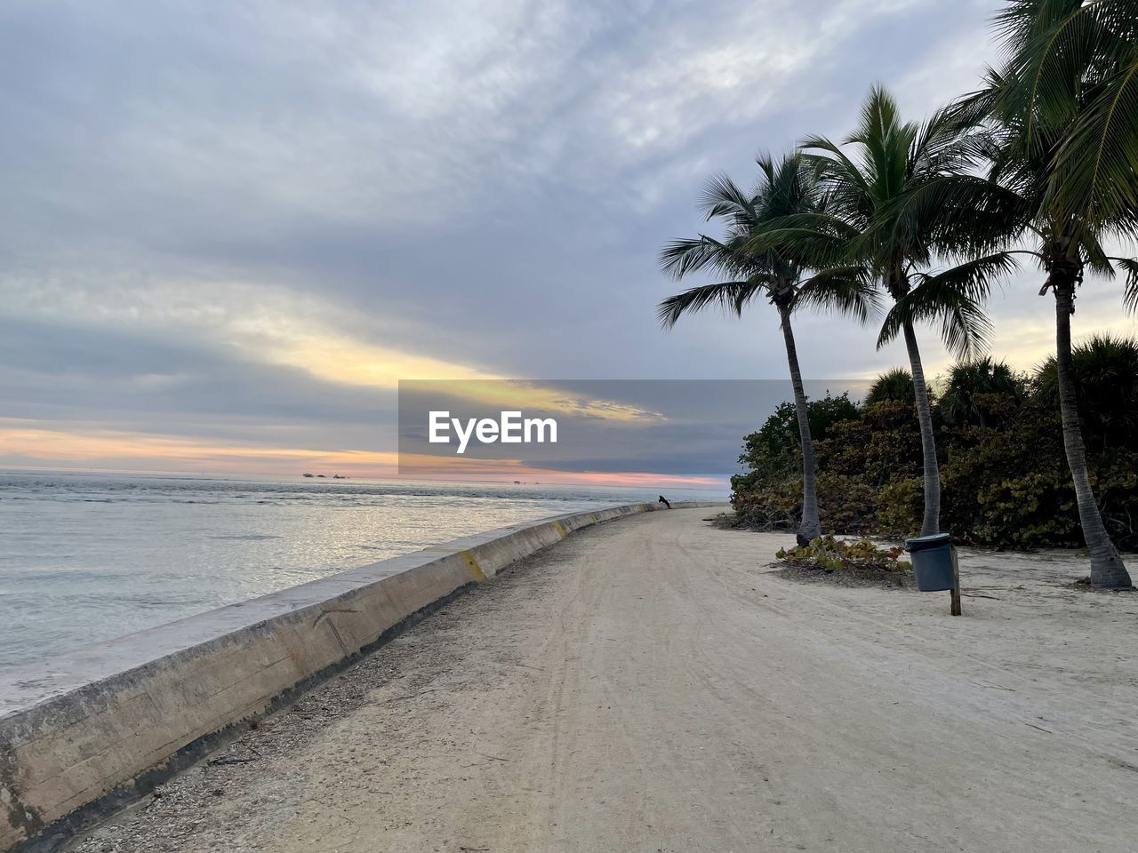 sky, palm tree, beach, sea, tropical climate, water, land, cloud, shore, tree, ocean, coast, beauty in nature, nature, scenics - nature, sand, body of water, plant, vacation, sunset, coconut palm tree, tranquility, tranquil scene, walkway, horizon over water, horizon, travel destinations, holiday, idyllic, trip, environment, travel, outdoors, bay, no people, tropical tree, coastline, tropics, island, seascape, landscape, tourism, wave, motion
