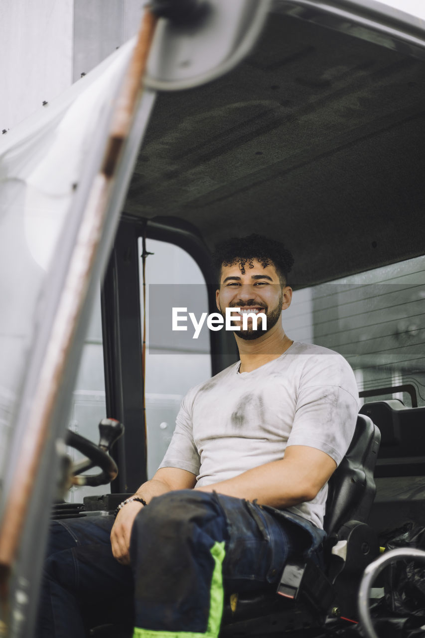 Happy young construction worker sitting in vehicle