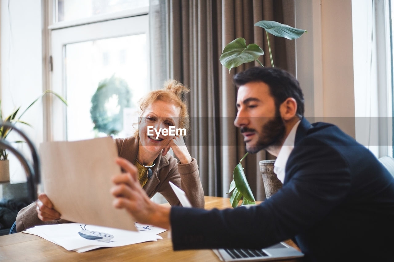 Smiling female illustrator showing drawing to male professional at office