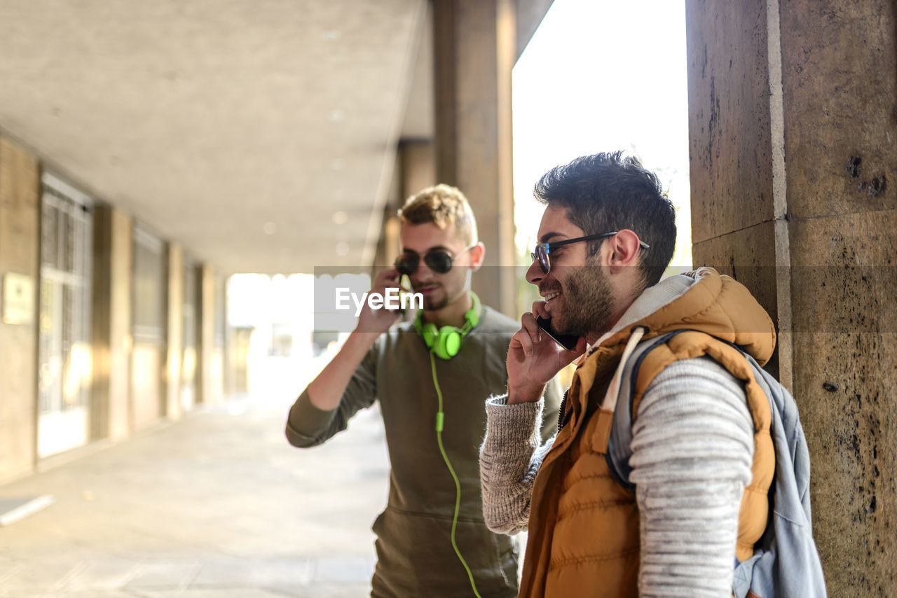 Male friends talking on phone while standing in city