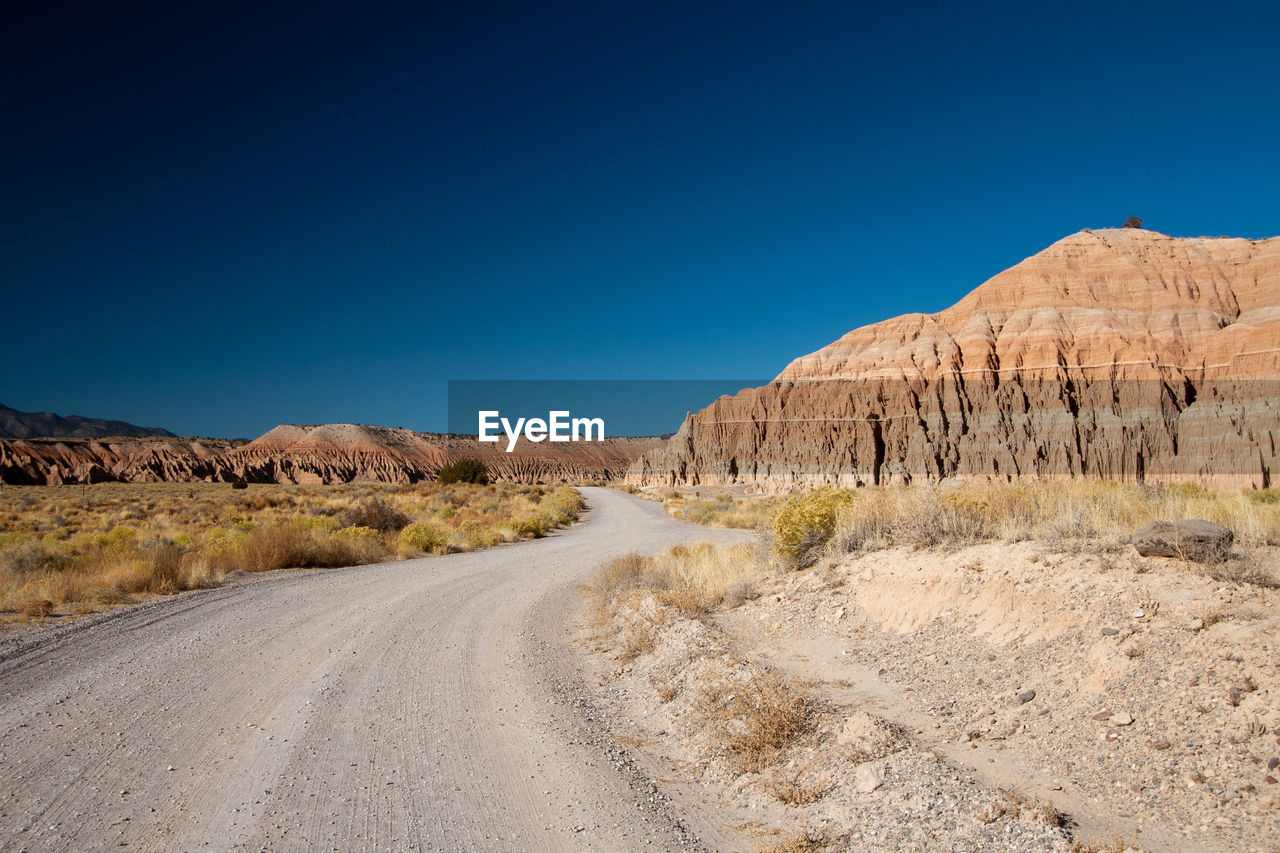 Road leading towards mountains against clear blue sky