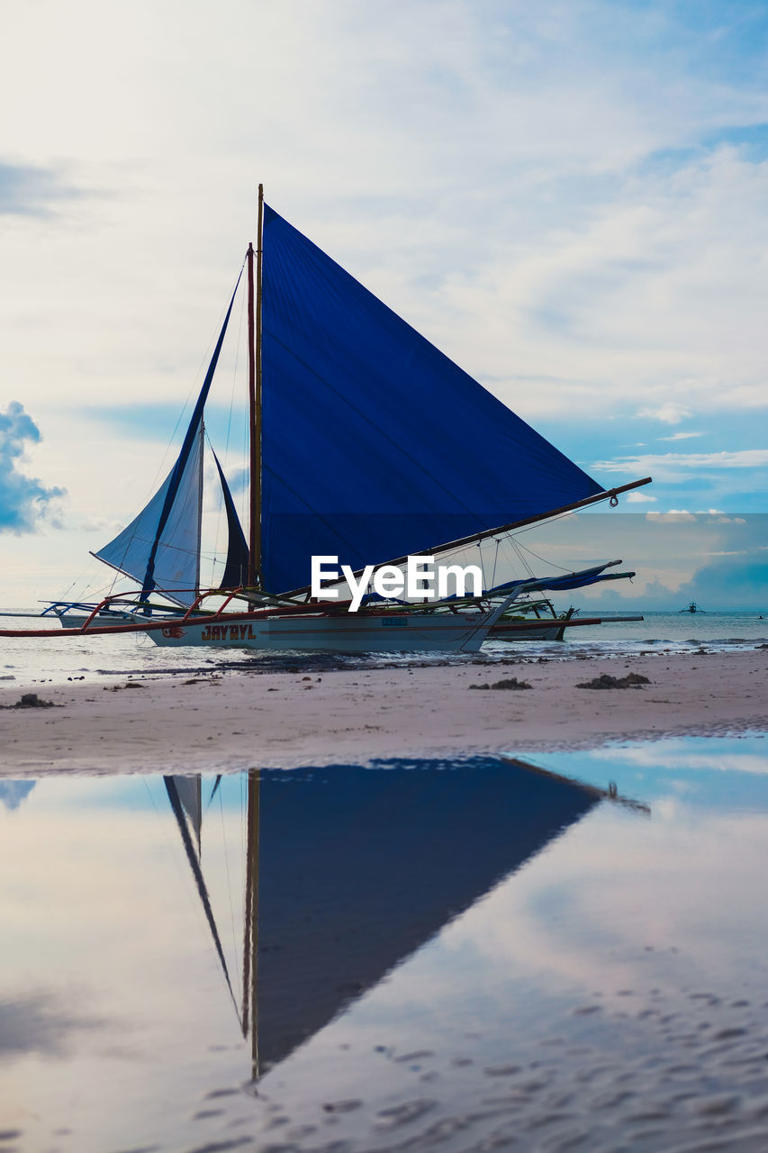 Sailboat moored on beach against sky