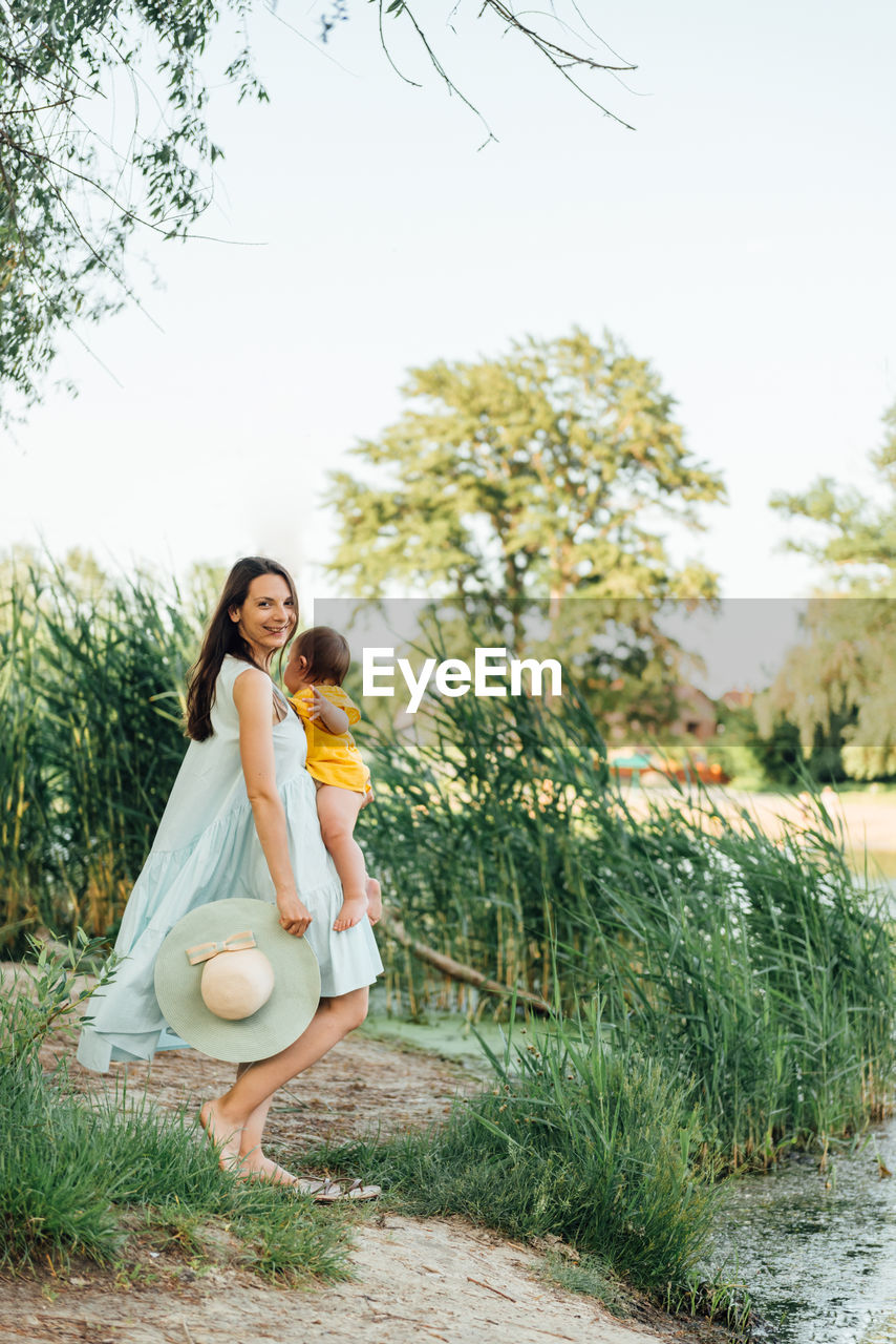 Woman carrying baby while standing against plants