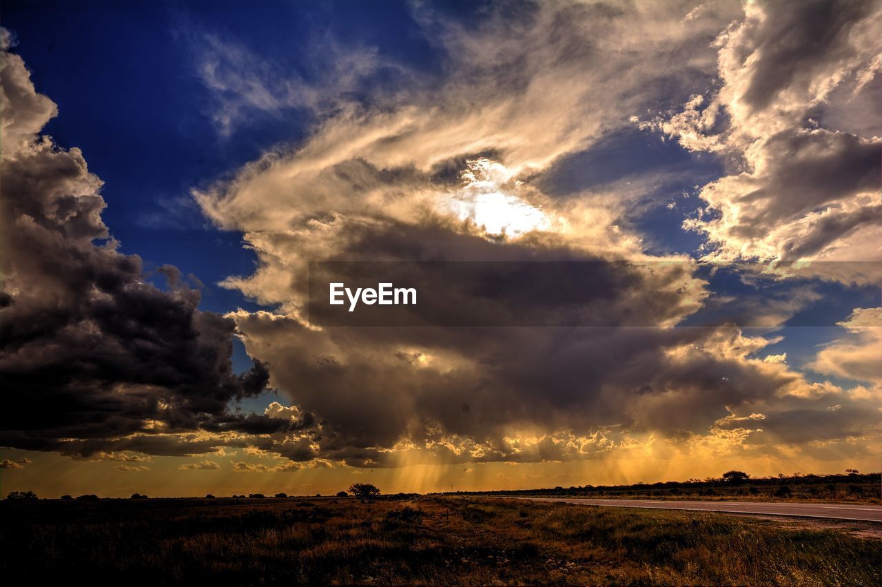 sky, cloud, environment, landscape, beauty in nature, horizon, nature, dramatic sky, sunset, sunlight, storm, dusk, cloudscape, evening, scenics - nature, land, no people, thunderstorm, outdoors, storm cloud, field, horizon over land, sunbeam, plant, blue, tranquility, awe, rural scene, summer, moody sky