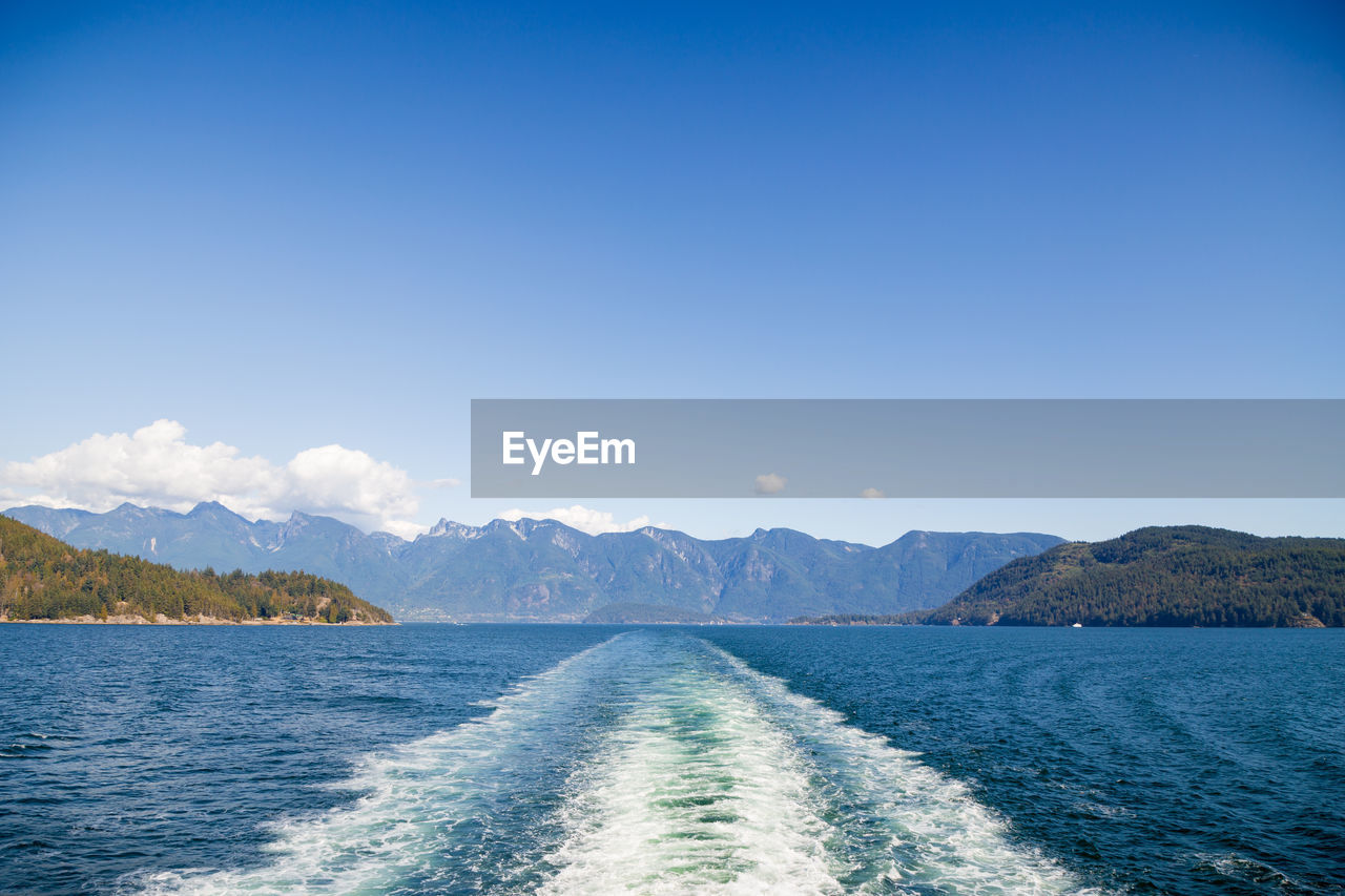 SCENIC VIEW OF SEA BY MOUNTAINS AGAINST CLEAR BLUE SKY