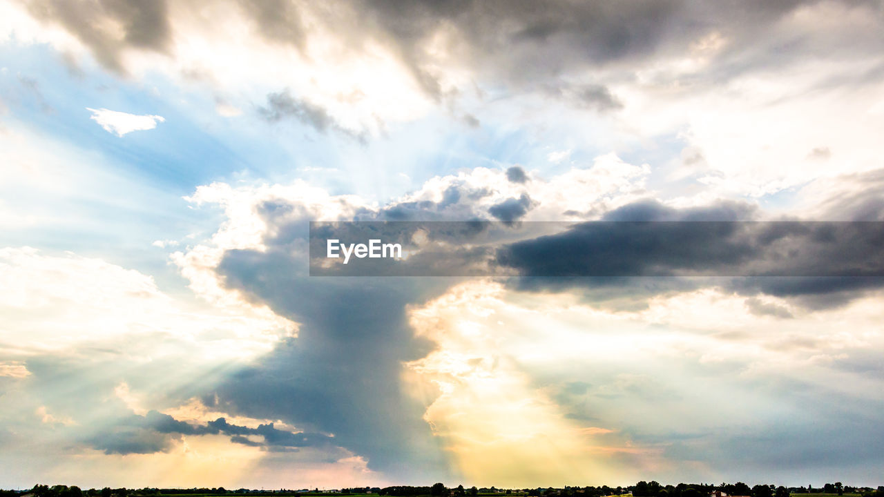 LOW ANGLE VIEW OF SUN STREAMING THROUGH CLOUDS IN SKY