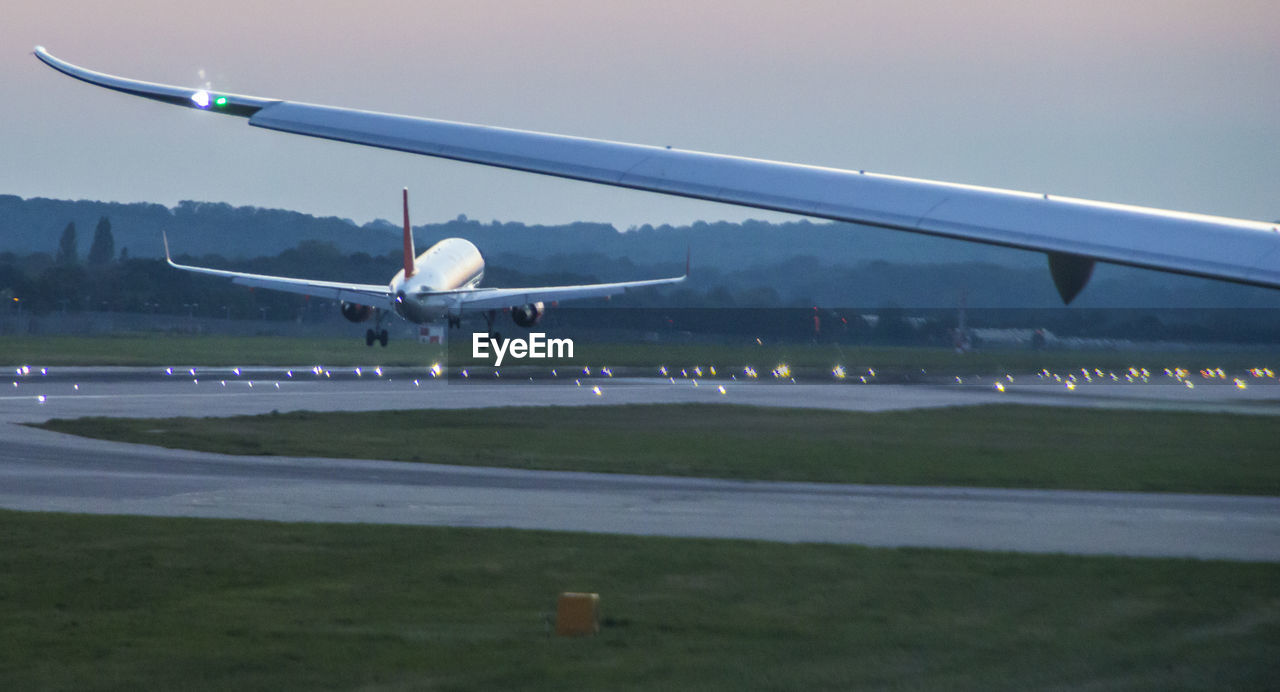 Cropped wing against airplane taking off from airport runway