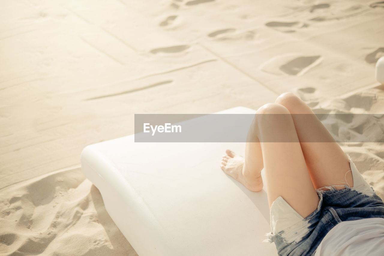 Low section of woman lying at beach during sunny day