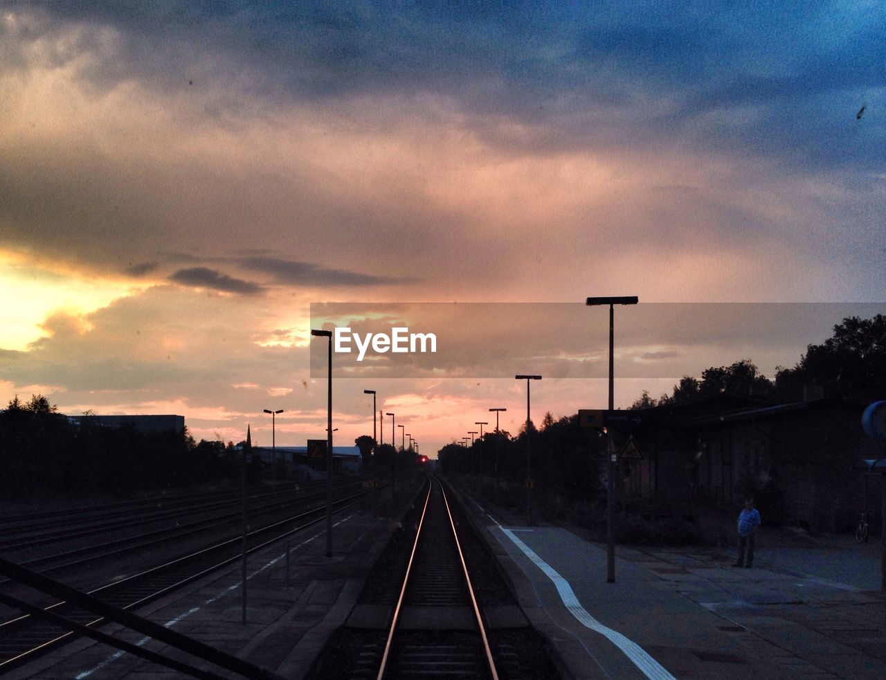 Railroad station platform against cloudy sky at sunset