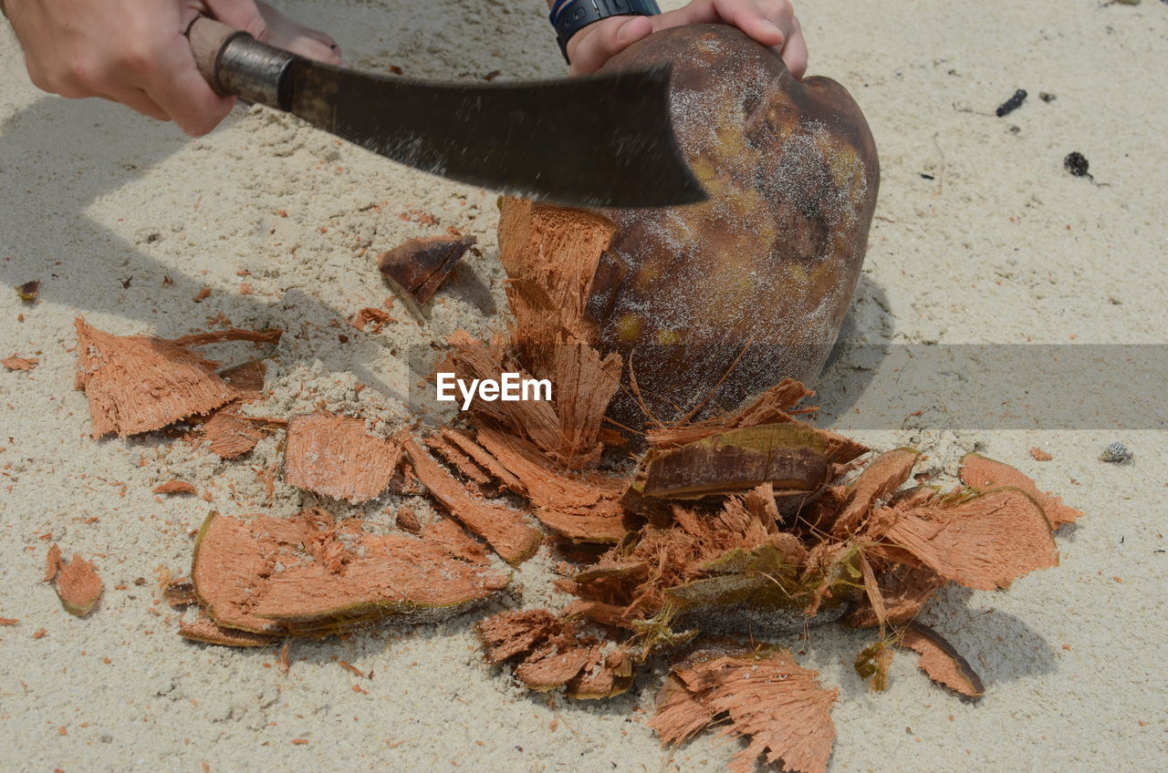 Cropped image of man peeling coconut with knife