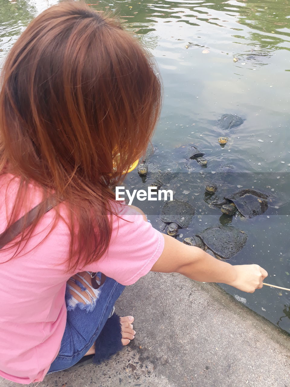 High angle view of girl crouching by water while holding stick