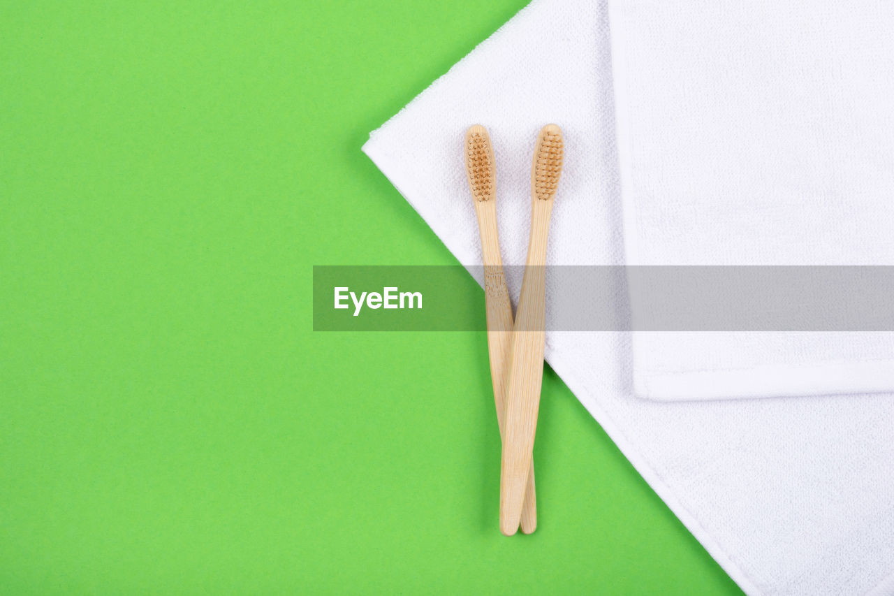 Top view of bamboo toothbrushes on white towels over green background. flat lay. 