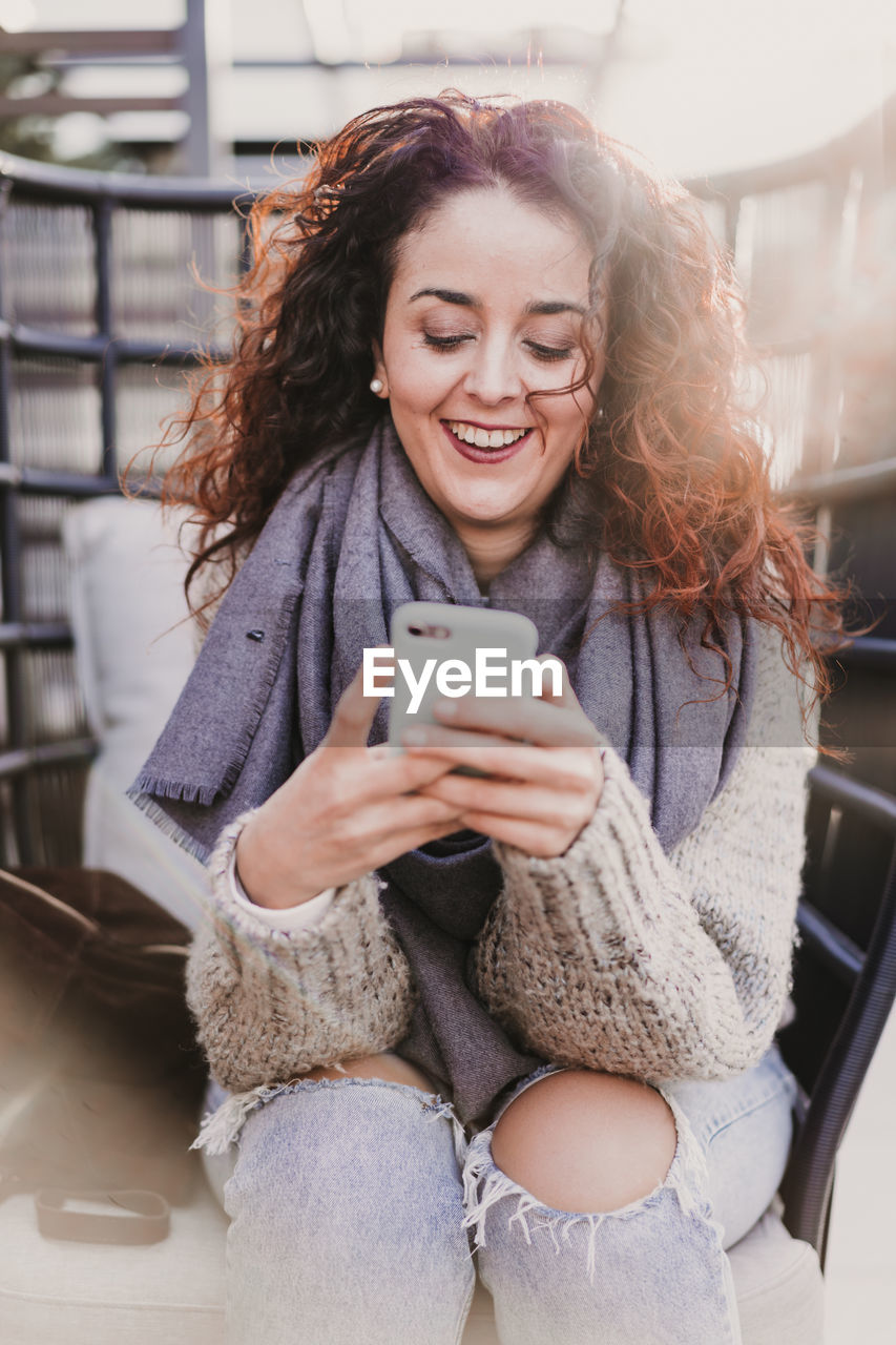 PORTRAIT OF SMILING WOMAN USING MOBILE PHONE IN A CAMERA