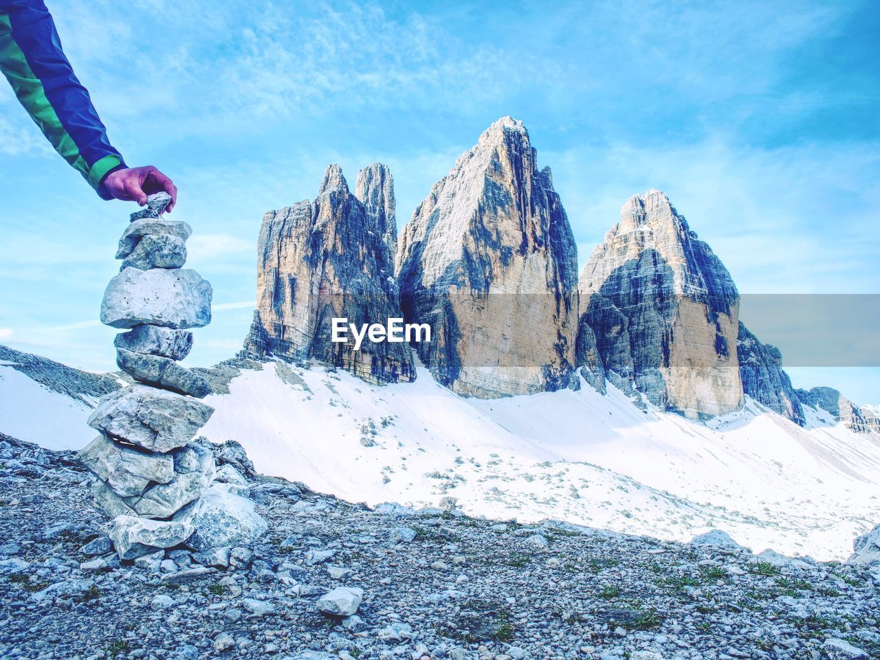 Alone hiker man at tre cime mountain massive building pyramid from pebbles. hand hold the last stone