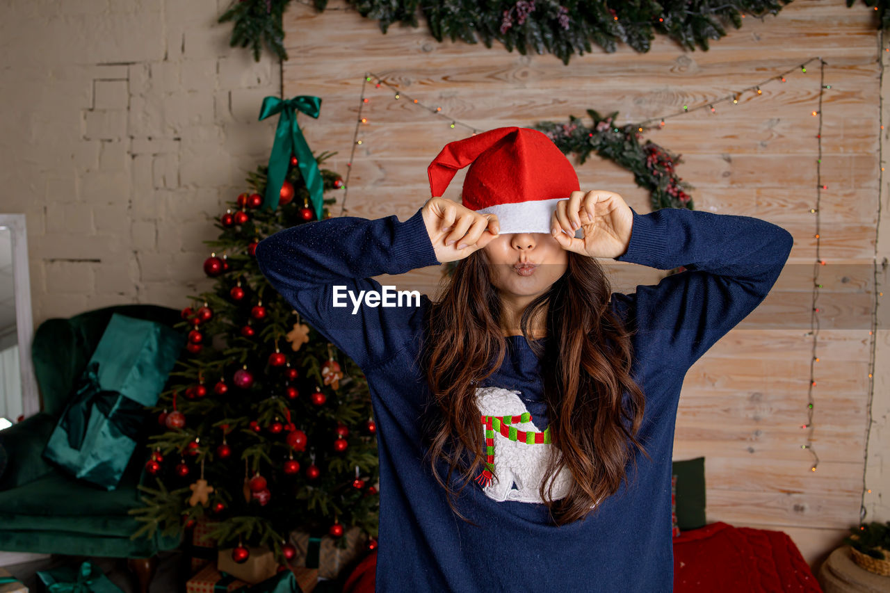 Happy asian girl in santa hat near christmas tree at home. christmas tree