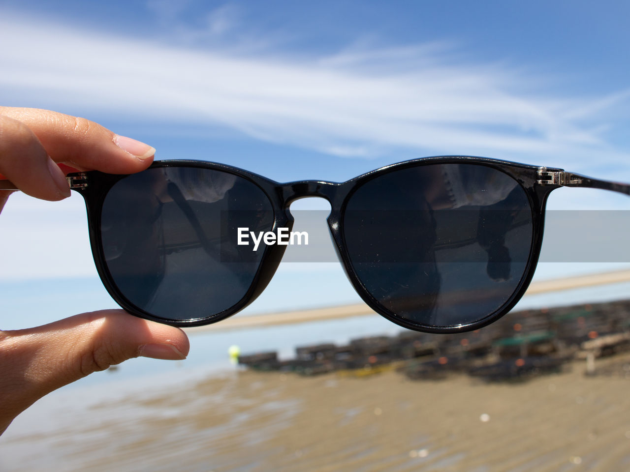 Cropped hand holding sunglasses at beach