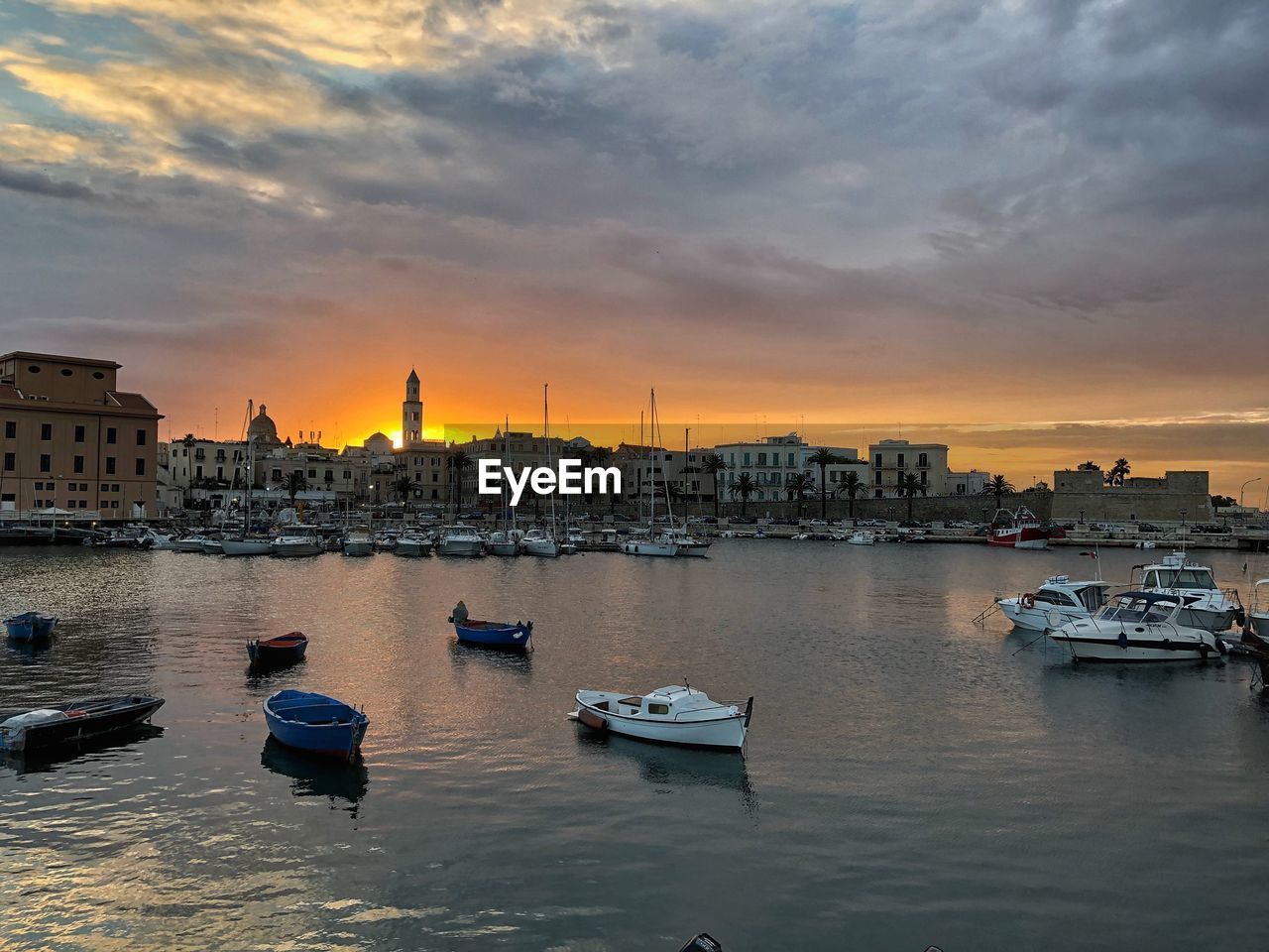 Sailboats moored in harbor against sky during sunset