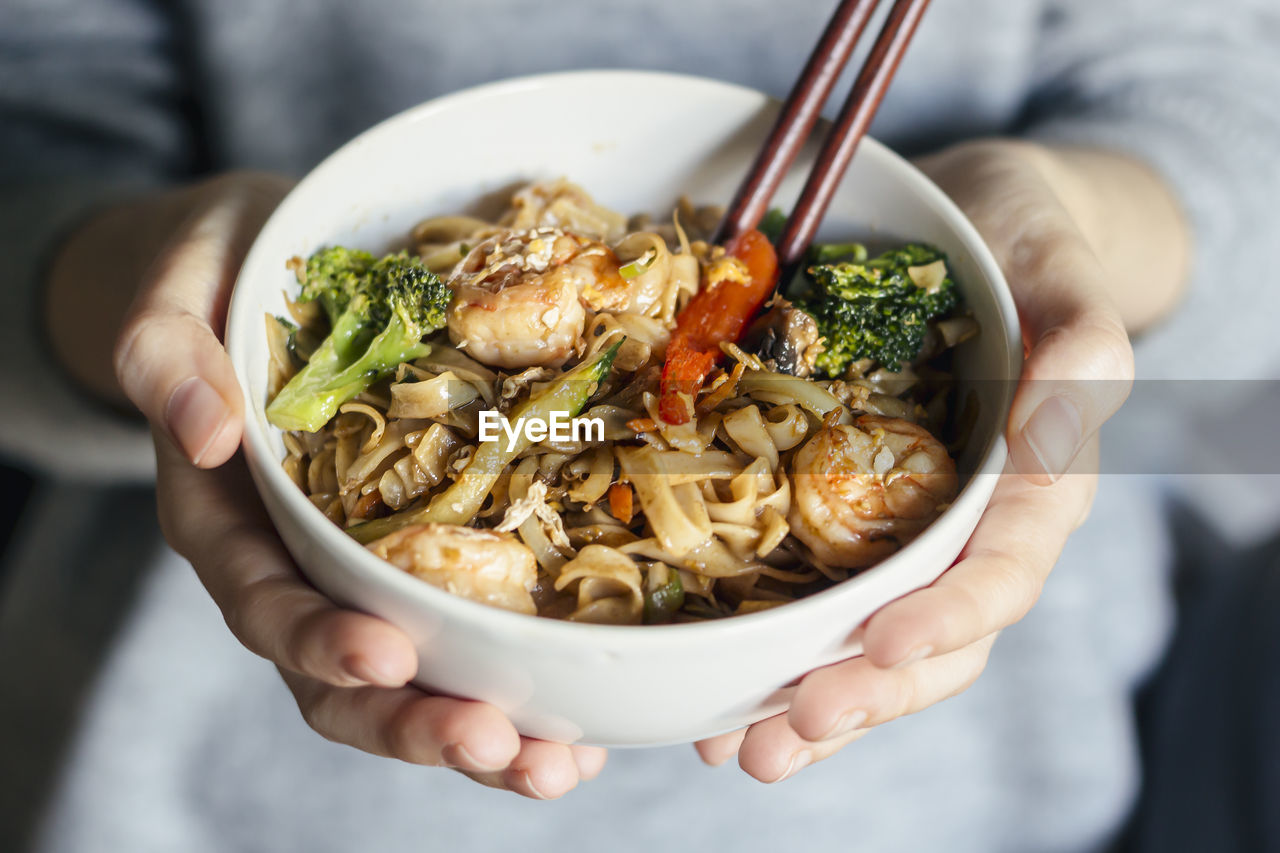 Female holding a bowl of seafood thai noodles