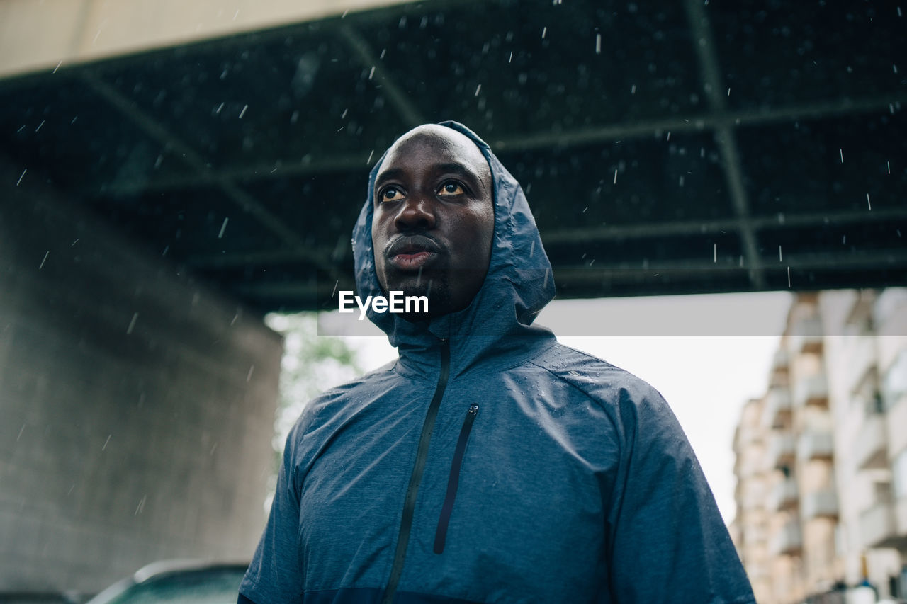 Low angle view of sportsman looking away while standing against bridge during rainy season