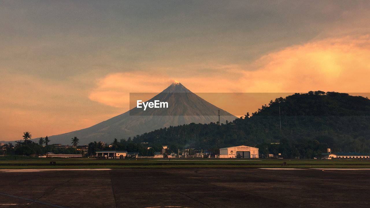 Scenic view of mountain and field against cloudy sky during sunset