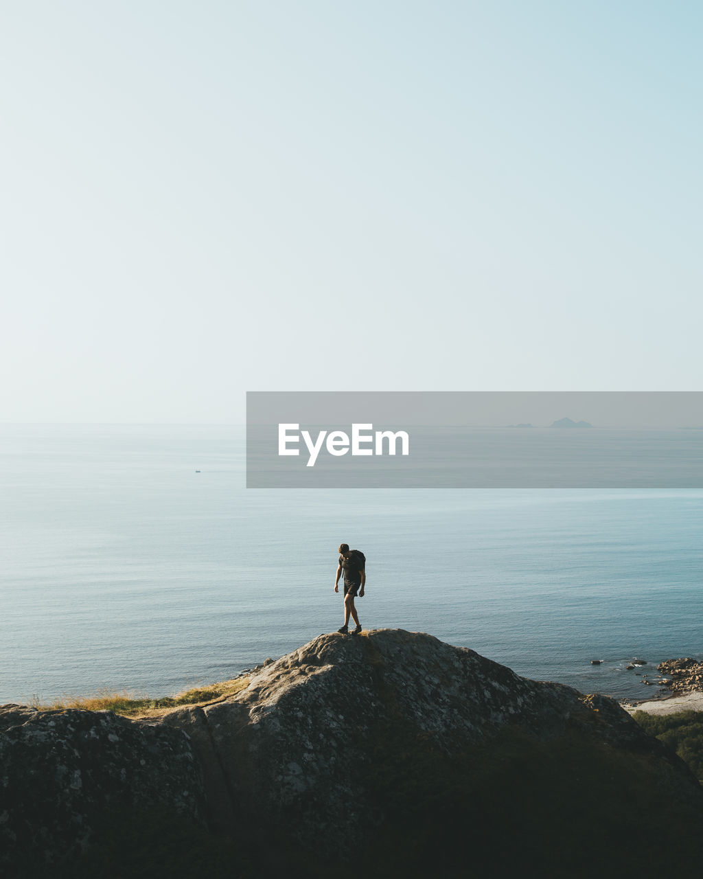 Man standing on rock by sea against clear sky