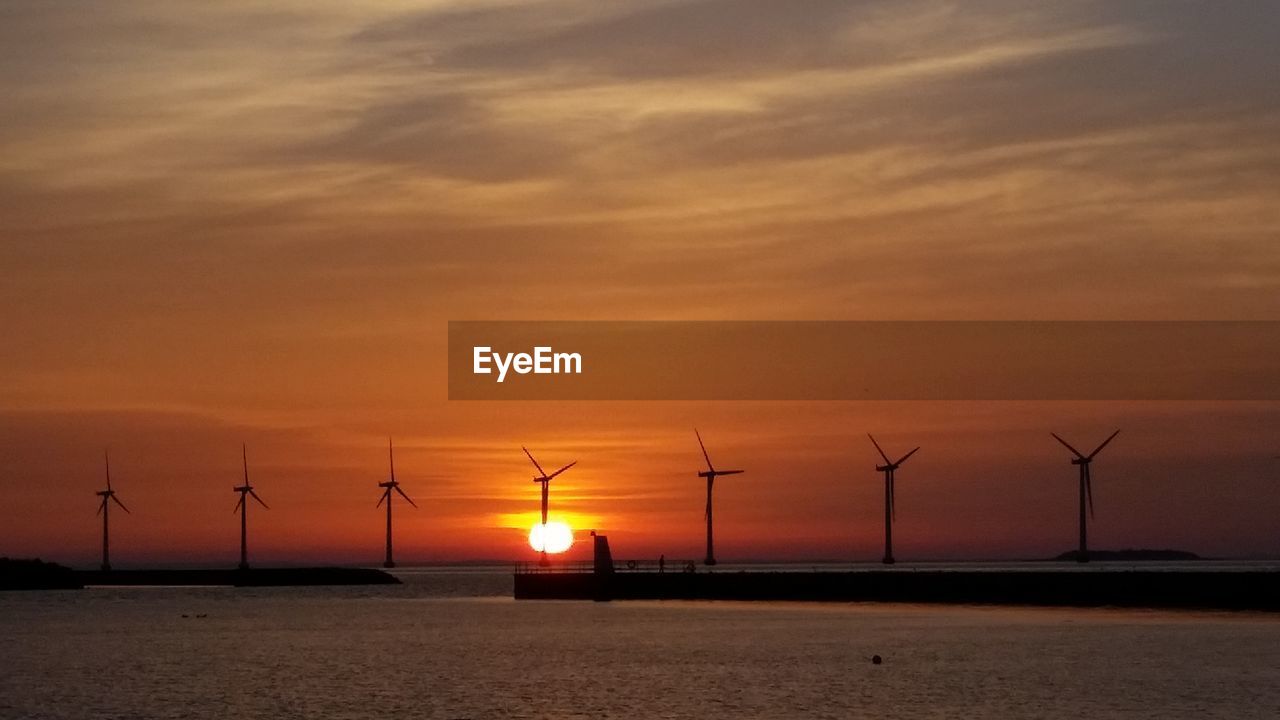 Silhouette wind turbines against orange sunset sky seen from amager strandpark
