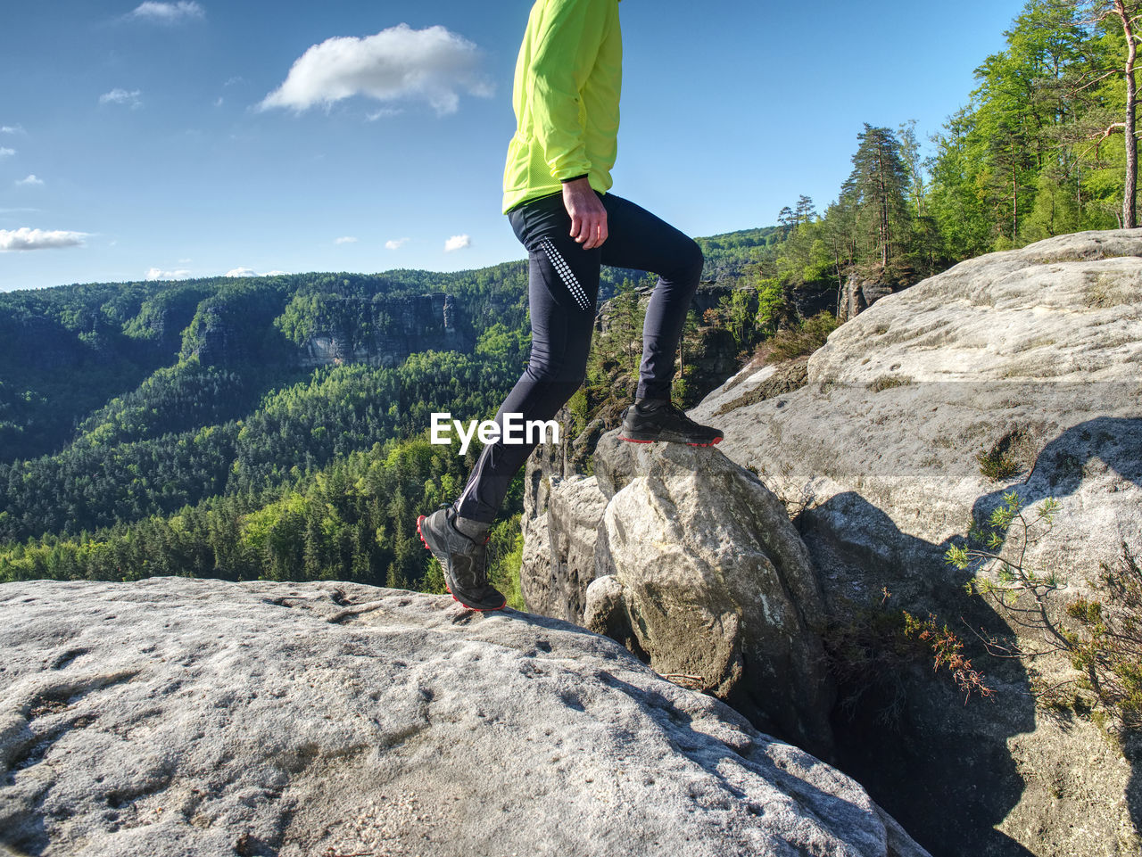 Fitness man trail runner running to rocky mountain top on cracked rocky block.