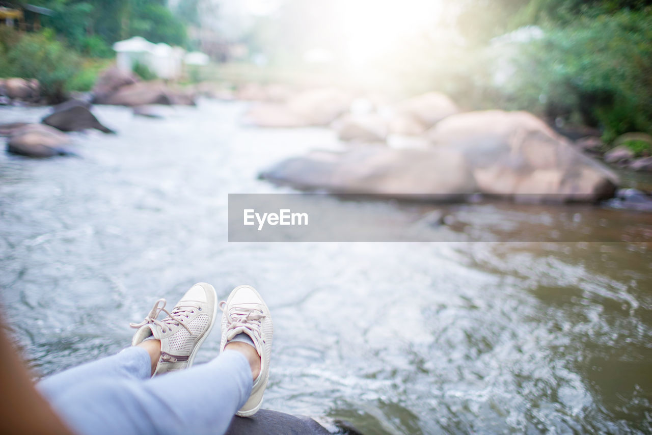 Low section of woman sitting by river on rock