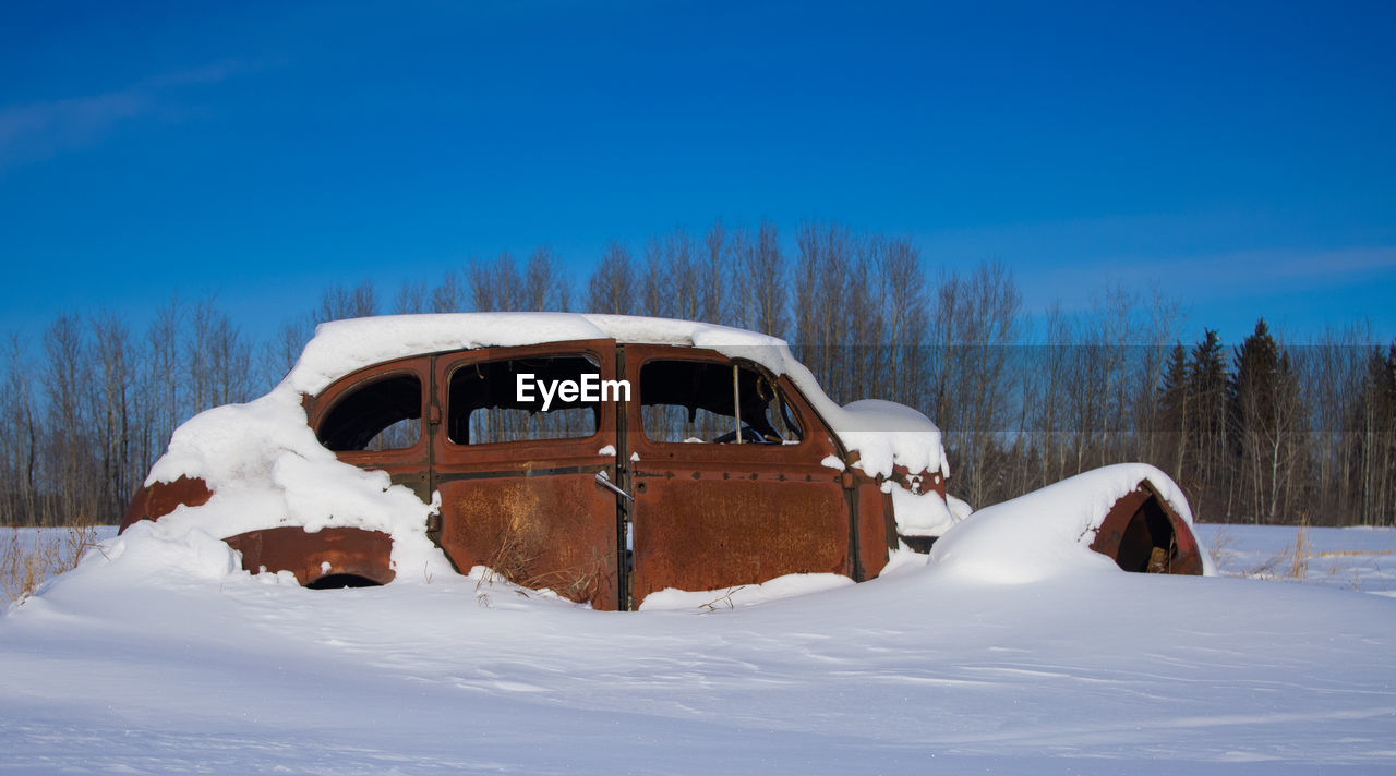 A snow covered, antique car slowly rusts away
