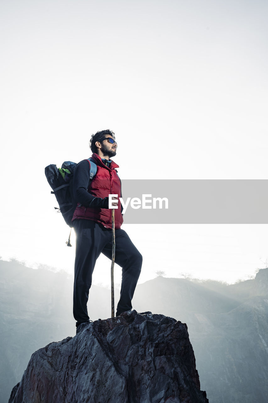 Young traveler in red snow jacket and a backpack standing on blue isolated background. 