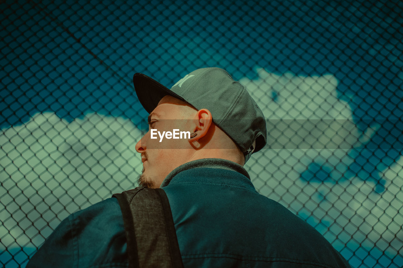 PORTRAIT OF MAN WEARING HAT AGAINST FENCE