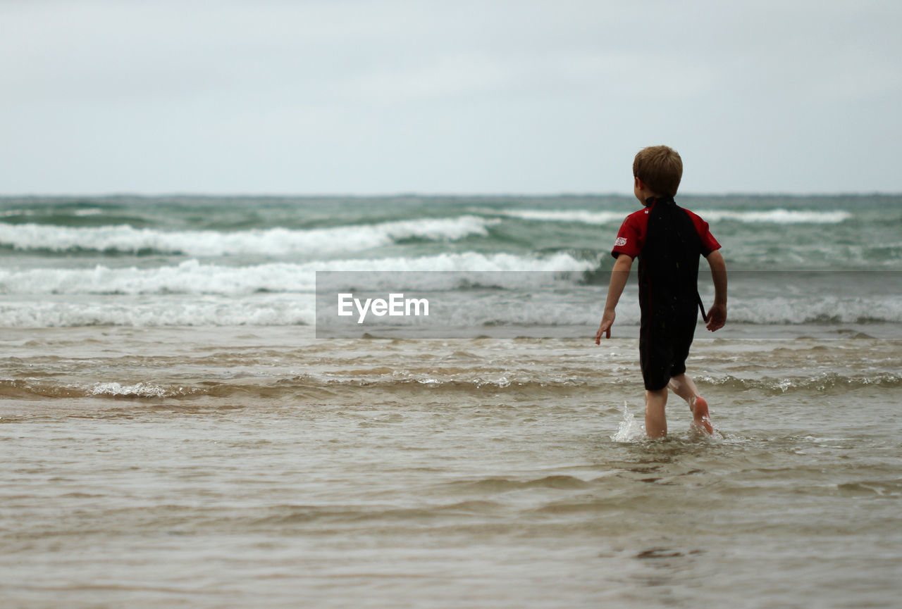 Rear view of boy walking in sea