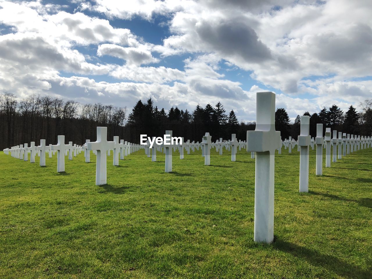 Panoramic low angle view of white crosses in cemetery against cloudy sky