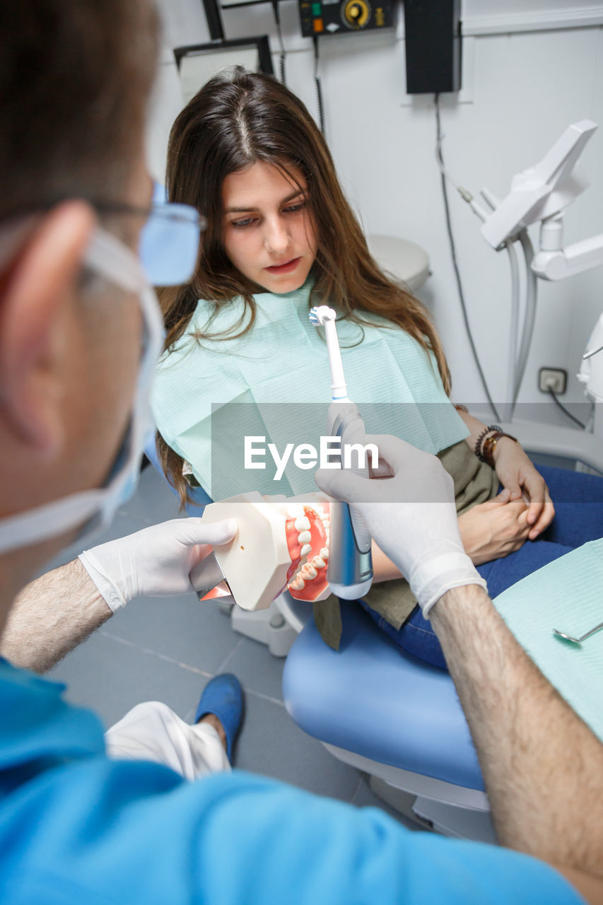 Professional doctor demonstration process of healthy teeth brushing to young woman sitting in chair