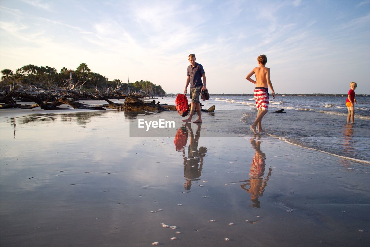 Father with boys on shore at beach in jekyll island against sky