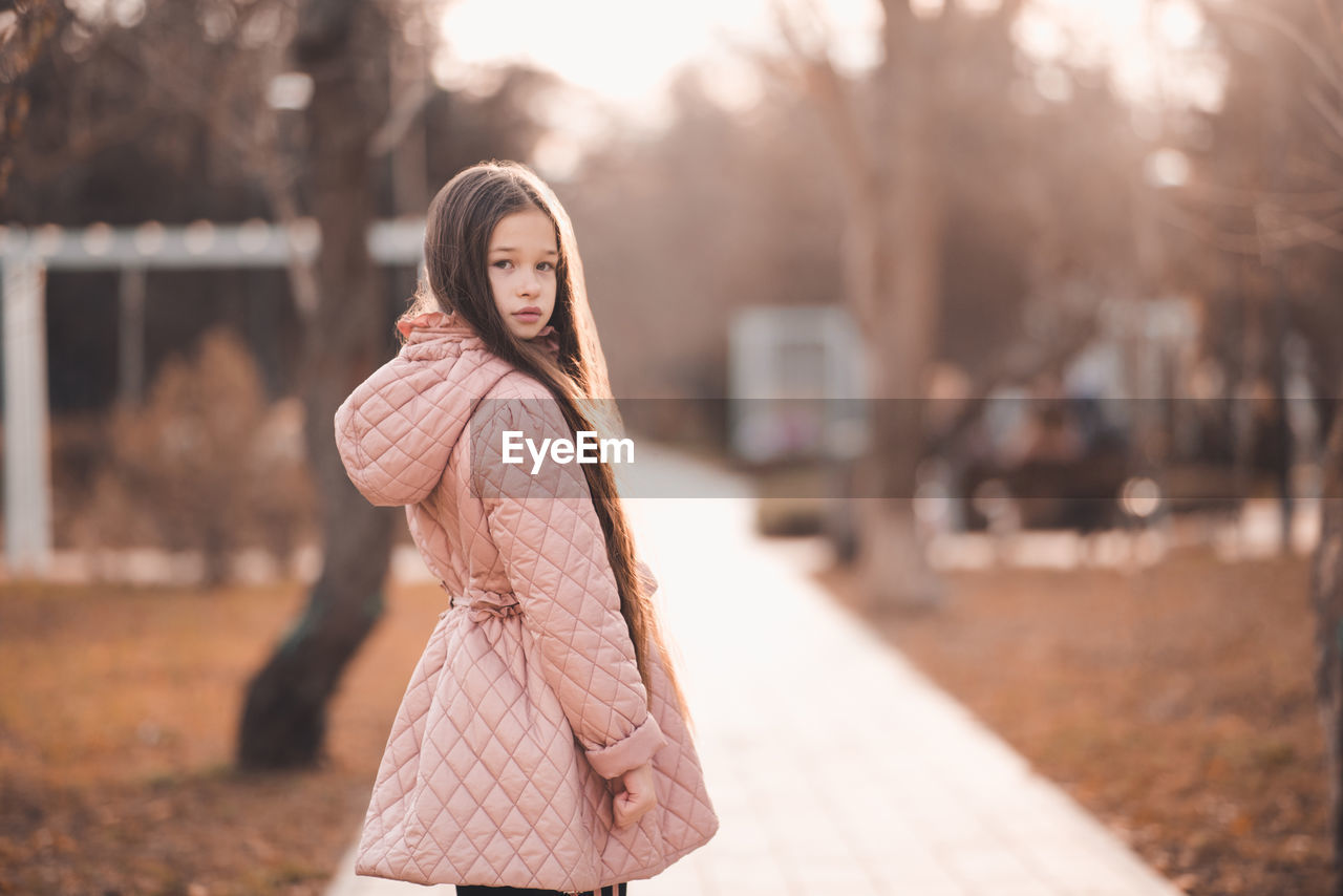 Portrait of stylish kid girl 10-12 year old with long blonde hair wear casual jacket in park outdoor